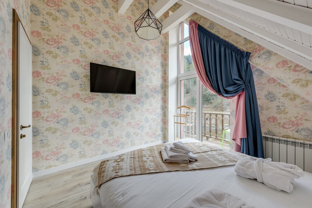 Bedroom with delicate floral wallpaper, exposed wood ceiling beams and balcony doors