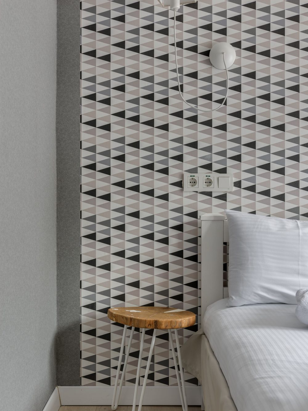 Bedroom corner finished in a neutral geometric wallpaper pattern with a small wooden stool