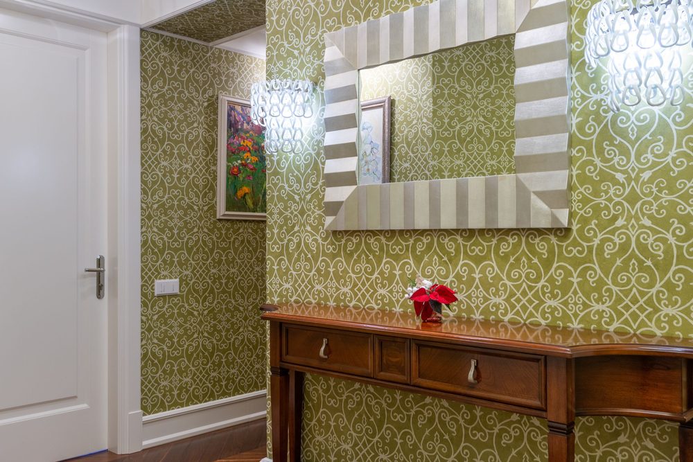 Classic hallway with ornate olive-green wallpaper, a wooden console and framed mirror