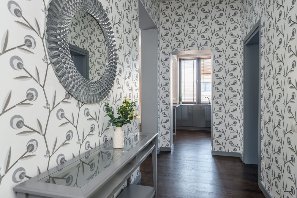 Warm hallway lined with botanical wallpaper, a round mirror and a console with greenery