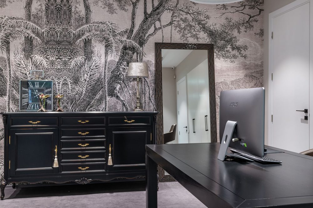 Moody home office with a grisaille tree-mural wallpaper, dark cabinet and desk