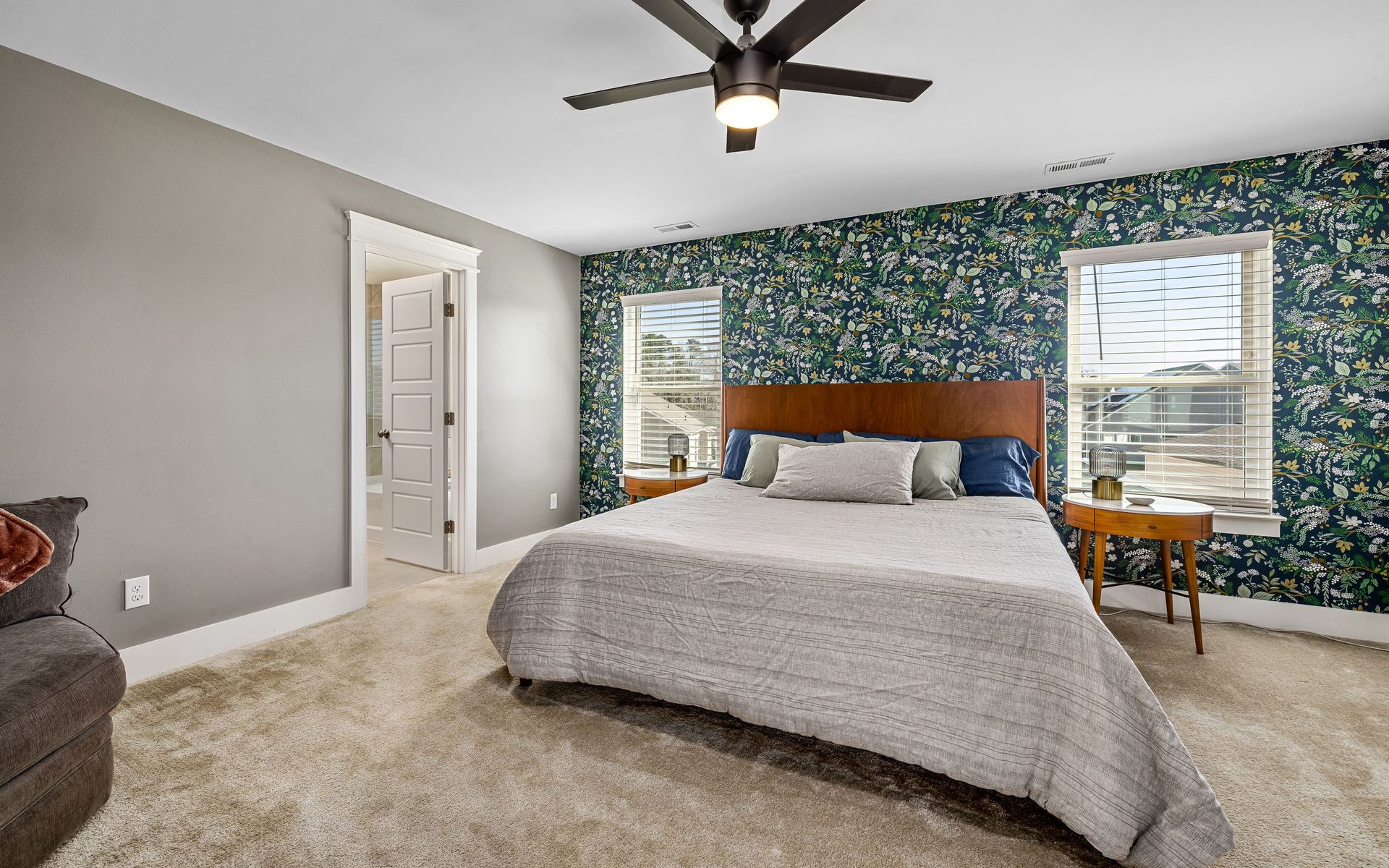 Bedroom with a botanical green wallpaper feature wall behind the bed, neutral bedding and bright windows