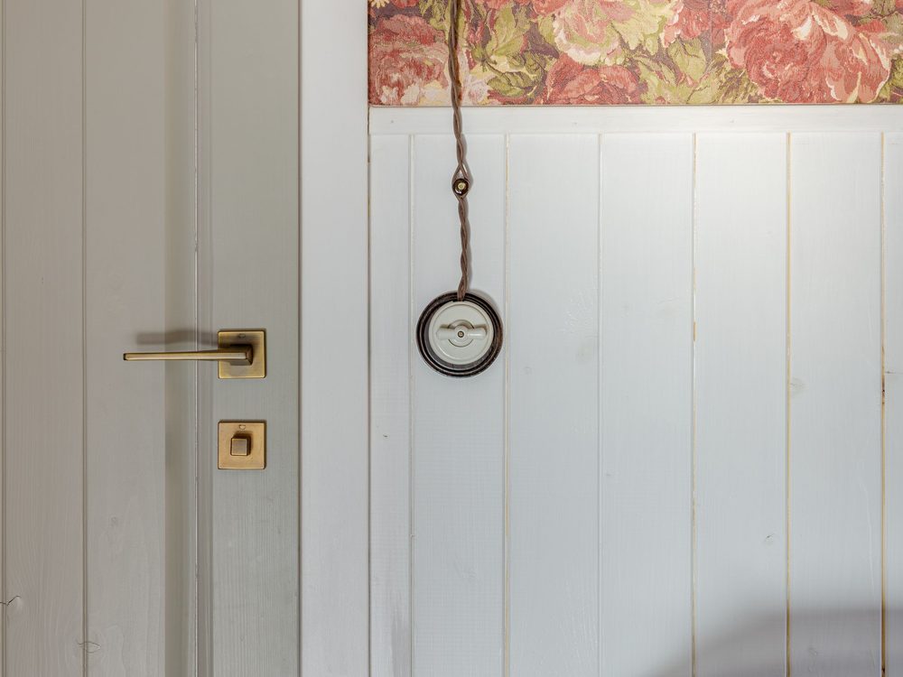 Detail of floral wallpaper meeting crisp white wainscot trim at a doorway